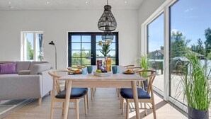 A modern dining area with a wooden table, blue chairs, and a hanging light fixture. - 2 bedroom amazing home in Rødby (Rødby)