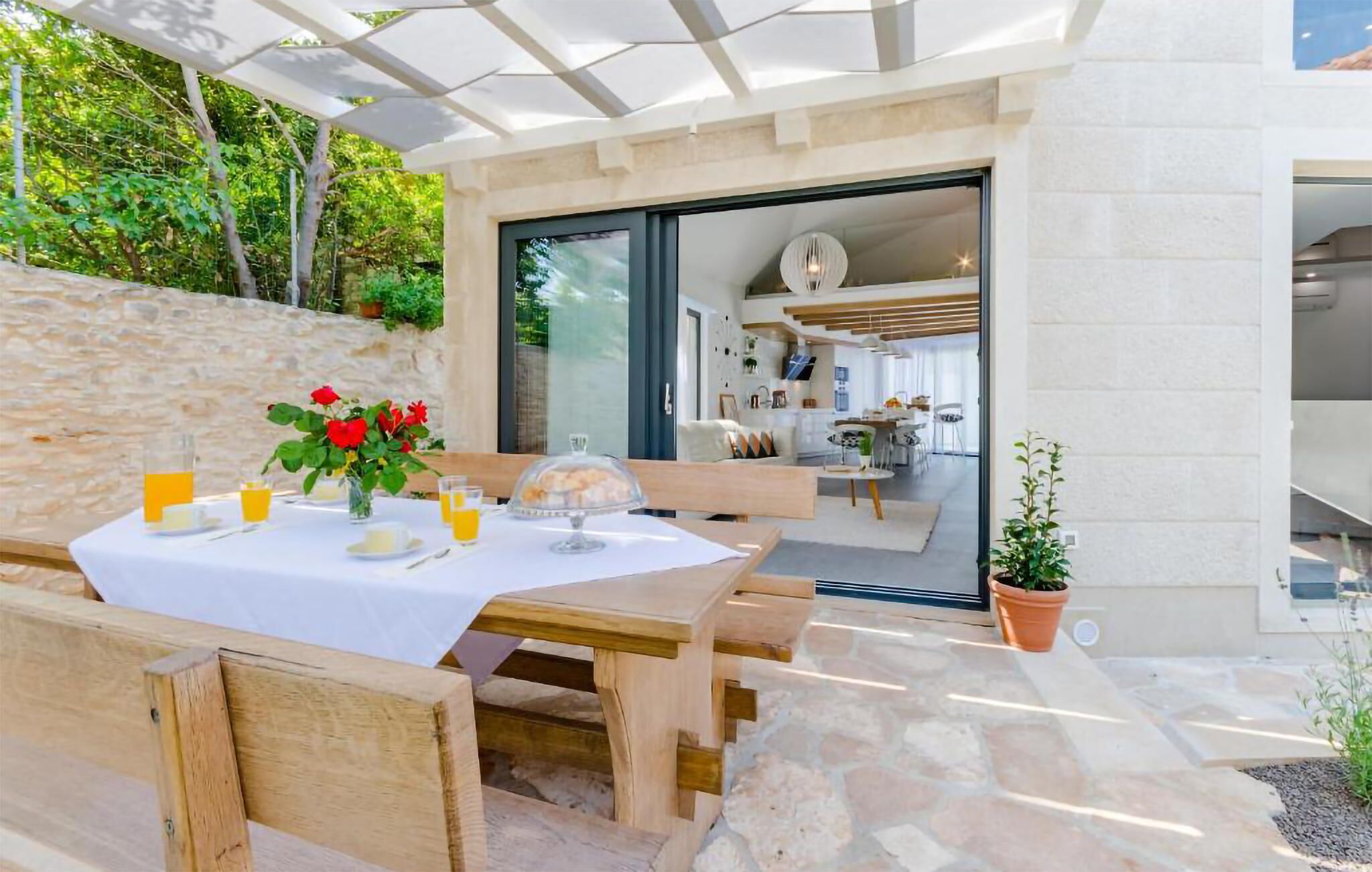 An outdoor dining area with a table set for two, a wooden bench, and a potted plant.