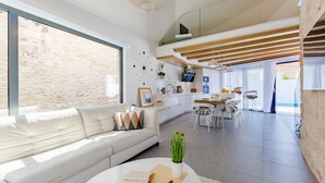 A modern living room with a white sofa, a dining area with a wooden table, and a kitchen with white cabinets. - Lovely home in Sutivan (Sutivan)