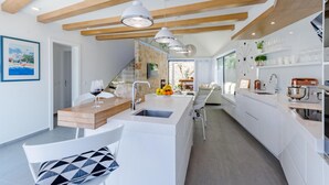 A modern kitchen with a central island, wooden beams on the ceiling, and a dining area with a white table and chairs. - Lovely home in Sutivan (Sutivan)