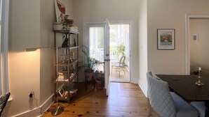 Une pièce dotée d’un plancher en bois, d’une bibliothèque, d’une table à manger avec des chaises, et d’une porte donnant sur un espace extérieur aménagé avec des chaises et une table.
