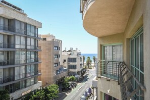 A multi-story building with balconies, a street in front, and a clear view of the sea.