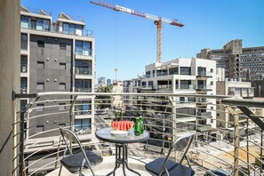 A balcony with a table, chairs, and a view of a construction site with a crane.