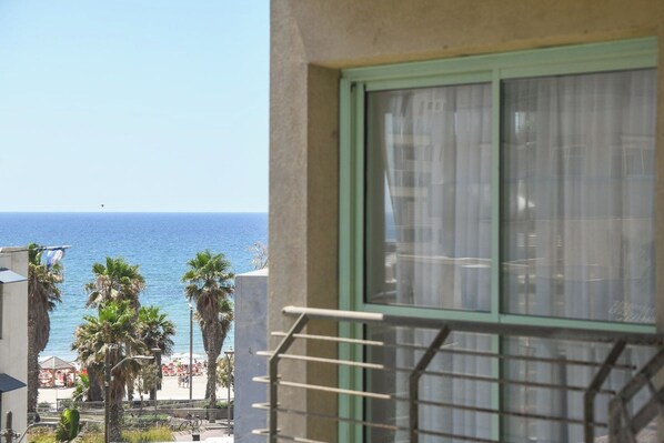 A balcony with a view of the sea, palm trees, and a beach.
