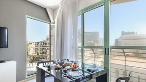 A dining area with a table set for four, large windows, and a view of the cityscape. - Mamad Modern 1BR w/ Style, City Views & Beach (Tel Aviv-Yafo)