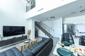 Un espace de vie moderne comprenant un téléviseur à écran plat, un canapé, une table à manger avec des chaises, ainsi qu’un coin cuisine équipé d’un réfrigérateur et d’un évier.