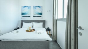 Une chambre d’hôtel moderne avec un grand lit, deux œuvres d’art accrochées au mur, une table de chevet avec une lampe et une fenêtre avec des rideaux.