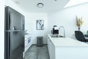 A modern kitchen with stainless steel appliances, a white countertop, and a small trash bin.