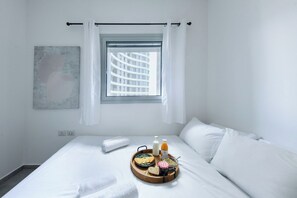 A hotel room with a bed, a window with curtains, a tray with breakfast items, and a wall-mounted artwork.