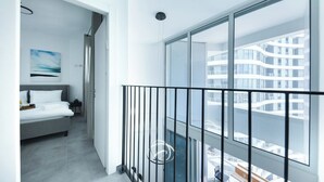 Una moderna camera d'albergo con balcone, un letto, un quadro e vista su un edificio sull'acqua.