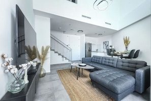 A modern living room with a grey sofa, a flat-screen TV, and a staircase leading to another level.
