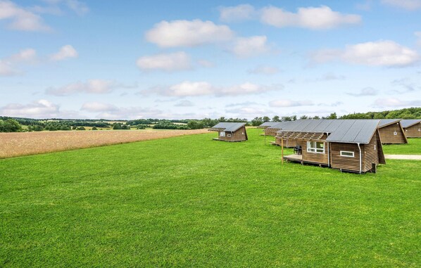 A row of wooden cabins with sloped roofs, set in a grassy field with a clear sky. - Awesome home in Kolding (Kolding)