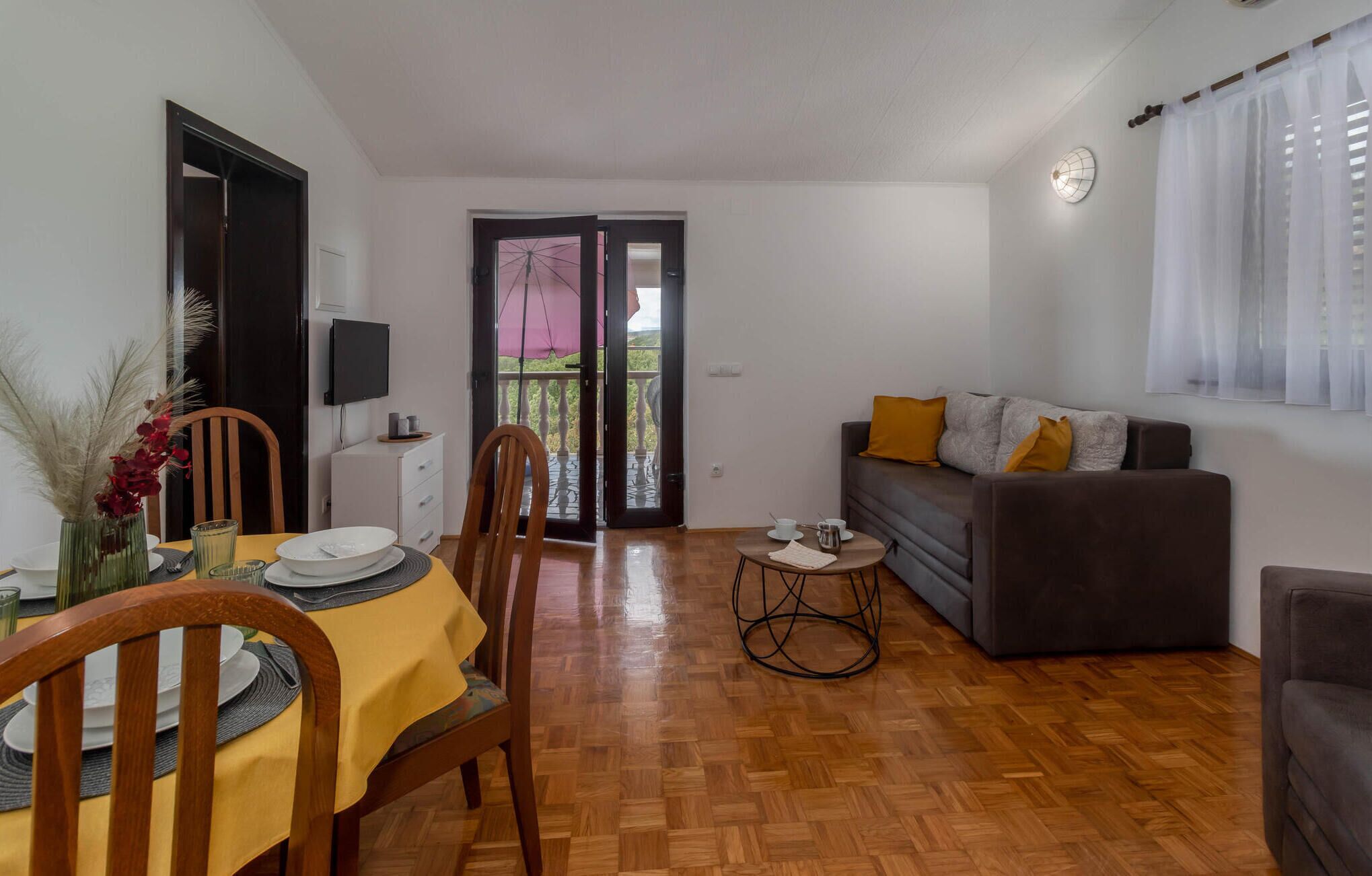 A living room with a sofa, a dining area with a table set for two, and a balcony with a view.