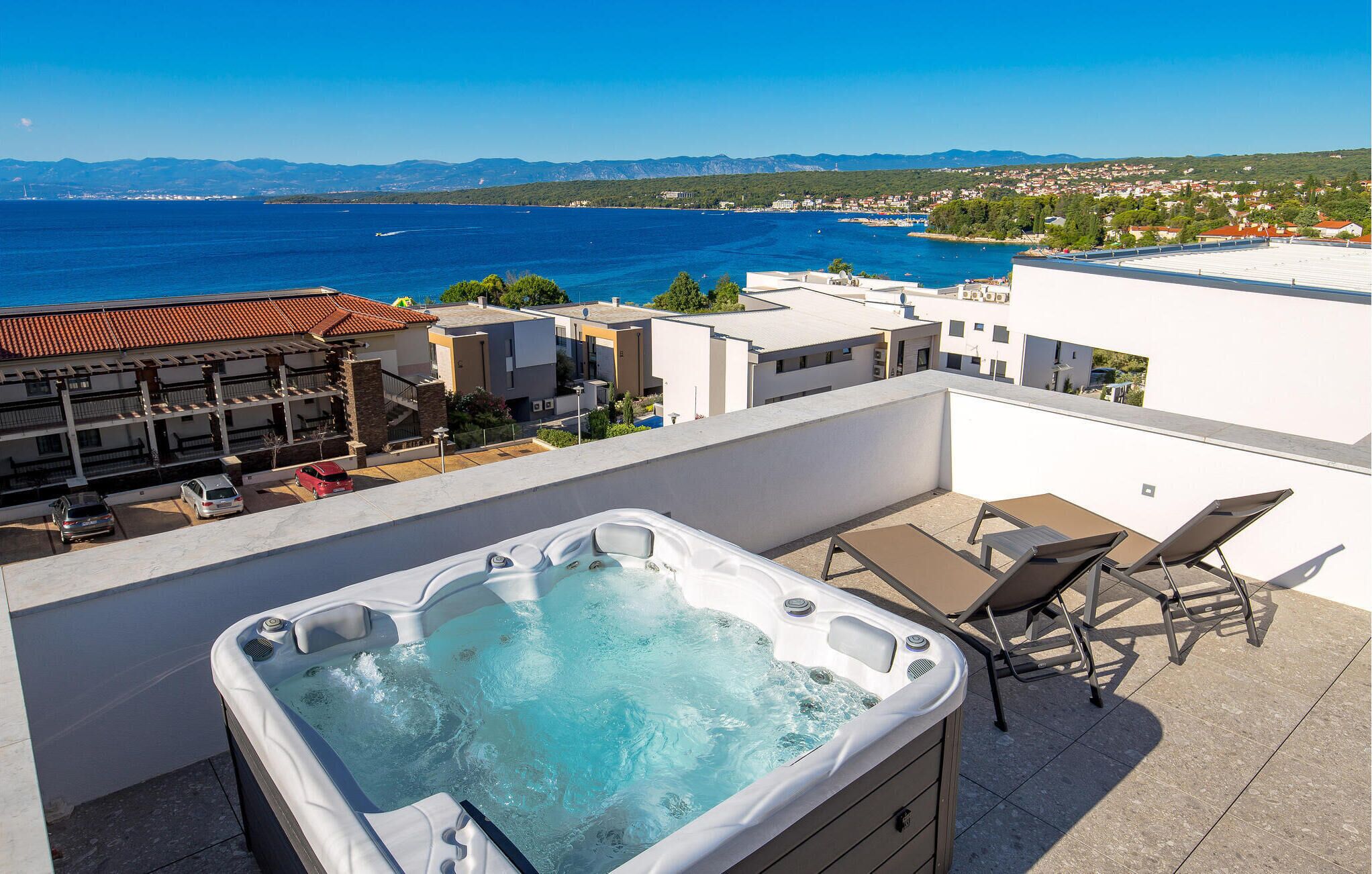 Eine Dachterrasse mit Whirlpool, Liegestühlen und Blick auf das Meer und ferne Berge.