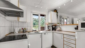 Une cuisine moderne avec des meubles blancs, une cuisinière encastrée et une fenêtre donnant sur un paysage verdoyant.