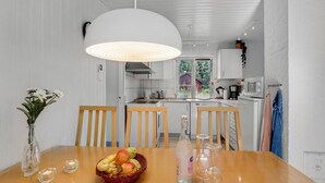 Une cuisine moderne avec des meubles blancs, un grand luminaire suspendu blanc et une table à manger agrémentée d’un panier de fruits et de verres.