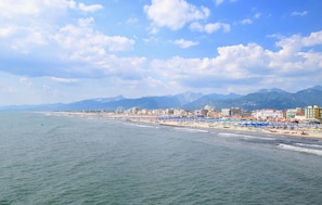 Eine Küstenstadt mit einem Strand, gesäumt von blauen Sonnenschirmen und Gebäuden im Hintergrund.