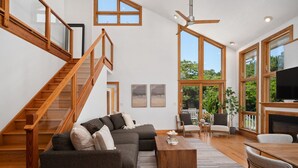A spacious living area with a wooden staircase, a sectional sofa, a coffee table, and a fireplace. - Indoor Hot Tub, Barrel Sauna, Pool, Natural Light! (Powells Point)