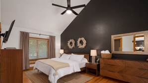 A bedroom with a bed, nightstands, a dresser, a ceiling fan, and two wall-mounted wreaths. - Indoor Hot Tub, Barrel Sauna, Pool, Natural Light! (Powells Point)