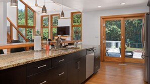 A modern kitchen with granite countertops, stainless steel appliances, and large windows offering a view of the outdoors. - Indoor Hot Tub, Barrel Sauna, Pool, Natural Light! (Powells Point)