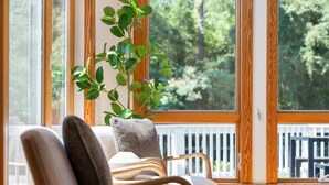 A wooden-framed window with a view of trees, a white chair with a cushion, and a potted plant. - Indoor Hot Tub, Barrel Sauna, Pool, Natural Light! (Powells Point)