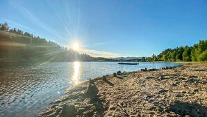 A beach with a clear view of the sun reflecting on the water, surrounded by trees and a distant mountain range. - Amazing home in Lunde with WiFi (Lunde)