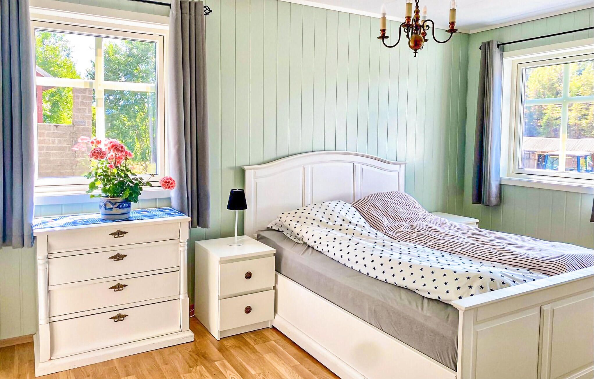A bedroom with a bed, nightstands, a dresser, a window with curtains, and a chandelier.
