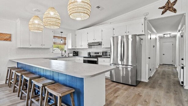A modern kitchen with white cabinets, a large island with stools, stainless steel appliances, and a decorative star on the wall. - Relaxed Beach Cottage, Steps to Sand, Near 30A & Pier Park (Panama City Beach)