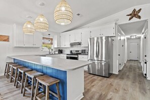 Une cuisine moderne avec des meubles blancs, un grand îlot central doté de tabourets, des appareils en acier inoxydable et une étoile décorative sur le mur.