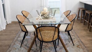 A dining area with a glass table surrounded by wicker chairs, a chandelier, and a patterned rug. - Relaxed Beach Cottage, Steps to Sand, Near 30A & Pier Park (Panama City Beach)