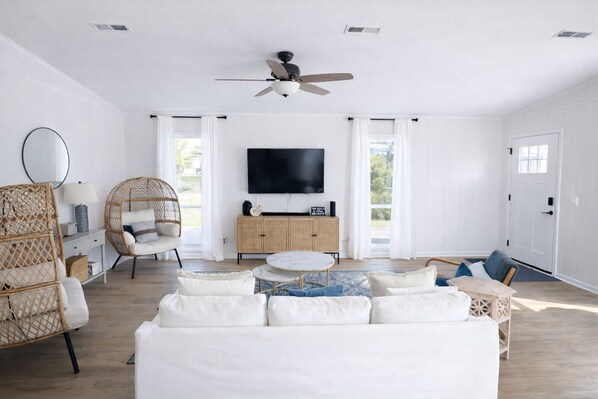 A spacious living room with a white sofa, wicker chairs, a round coffee table, and a ceiling fan. - Relaxed Beach Cottage, Steps to Sand, Near 30A & Pier Park (Panama City Beach)