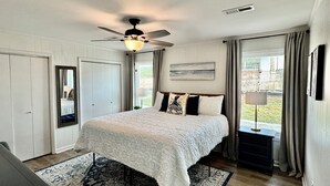 A bedroom with a bed, a ceiling fan, a window with curtains, and a view of the outdoors. - Relaxed Beach Cottage, Steps to Sand, Near 30A & Pier Park (Panama City Beach)