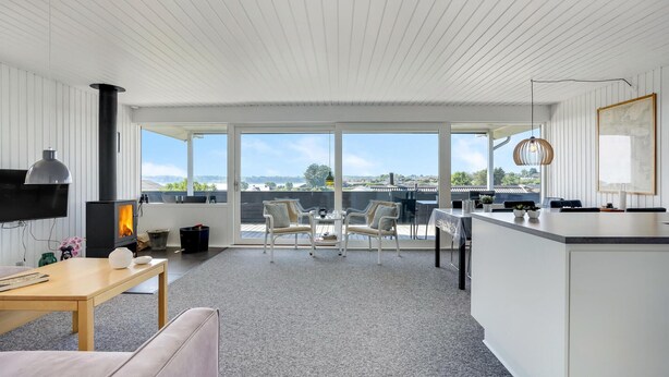 A modern kitchen with a large island, a dining area with a table and chairs, and a view of the countryside through large windows. - 3 bedroom awesome home in Hejls (Hejls)