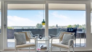 A room with two chairs facing a sliding glass door, a small table with a lamp, and a view of a body of water and buildings. - 3 bedroom awesome home in Hejls (Hejls)