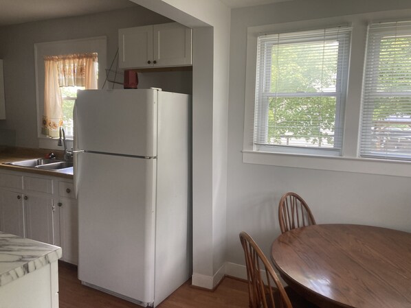 A kitchen with white cabinets, a refrigerator, a dining table with chairs, and a window with blinds. - Convenient to Knoxville, Dollywood, Univ. of TN (Alcoa)
