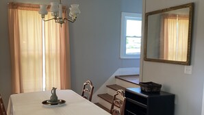 Un espace repas avec une table dressée pour quatre personnes, un lustre, un miroir et un escalier menant à un niveau supérieur.