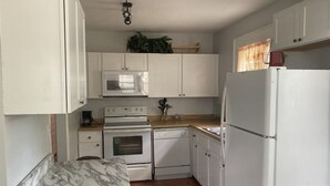 Une cuisine compacte avec des meubles blancs, un plan de travail en marbre, un four à micro-ondes, un four traditionnel, un lave-vaisselle et un réfrigérateur.