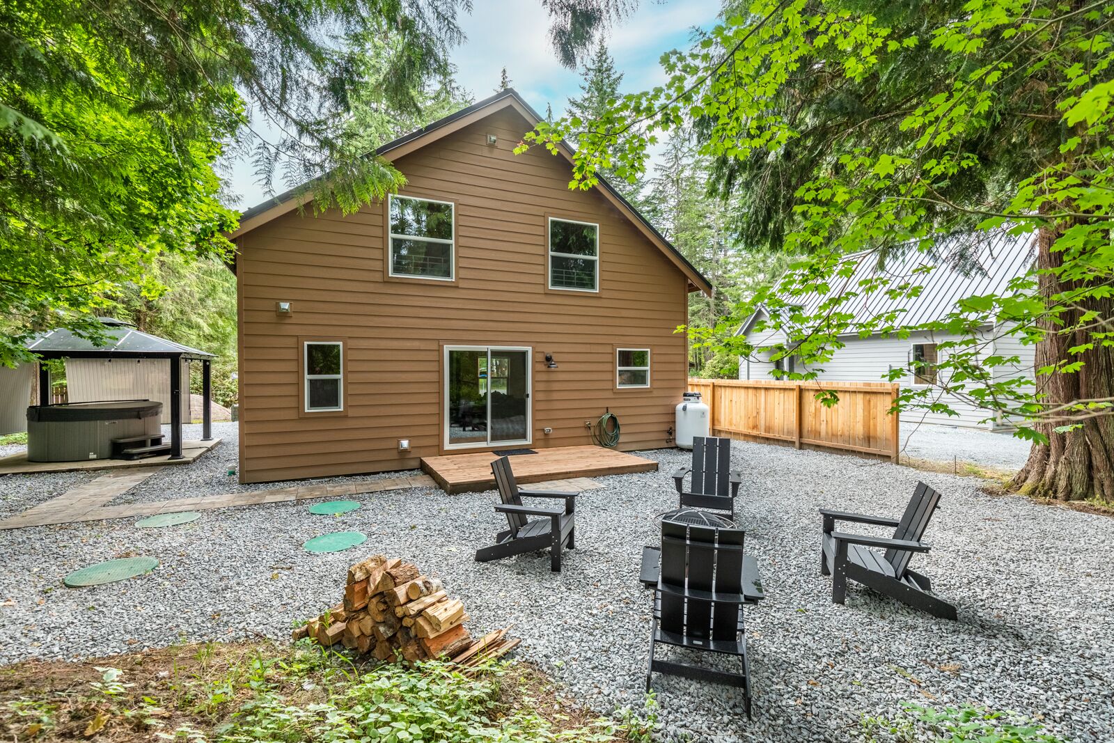 Une maison en bois à deux étages, dotée d’un patio comprenant un barbecue et des sièges.