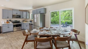 Une cuisine moderne avec des meubles gris, des appareils en acier inoxydable et un coin repas doté d’une grande table pouvant accueillir six personnes.