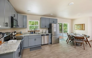 A modern kitchen with grey cabinets, stainless steel appliances, and a dining area with wooden chairs and a table.