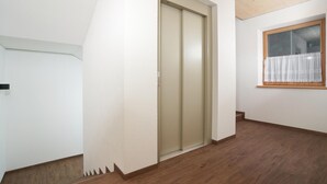 Een gang met een houten vloer, een schuifdeur en een raam met een witte gordijn.