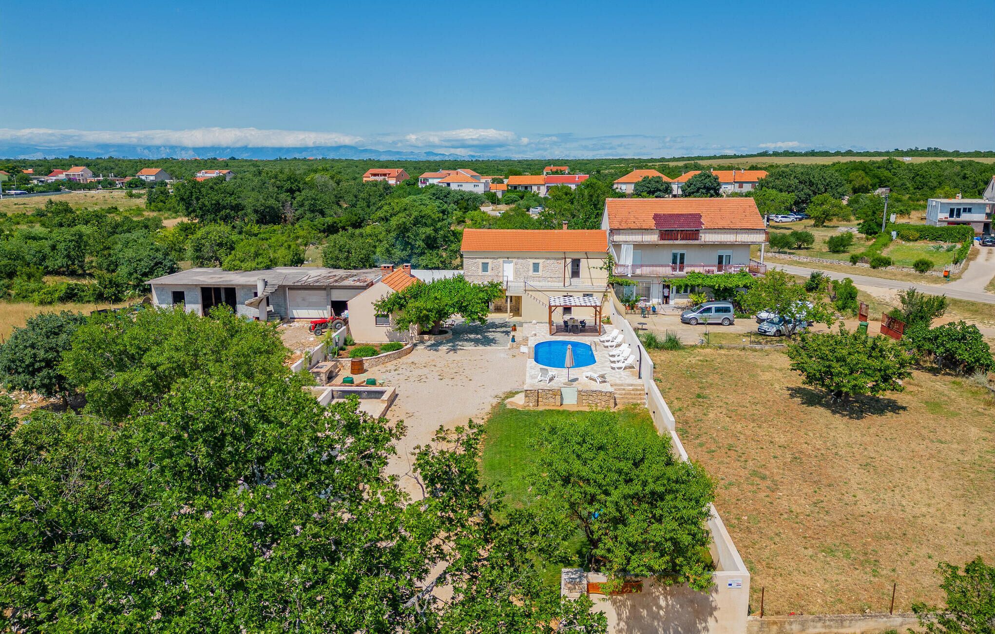 Un quartier résidentiel avec une grande maison dotée d’une piscine, entourée de verdure et d’autres habitations.