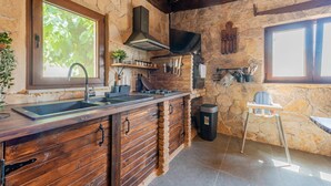 Une cuisine rustique avec un mur en pierre, des armoires en bois, une cuisinière à gaz et une fenêtre donnant sur un paysage verdoyant.
