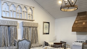 Un salon avec un canapé beige, des coussins à motifs, un fauteuil ancien et un lustre.