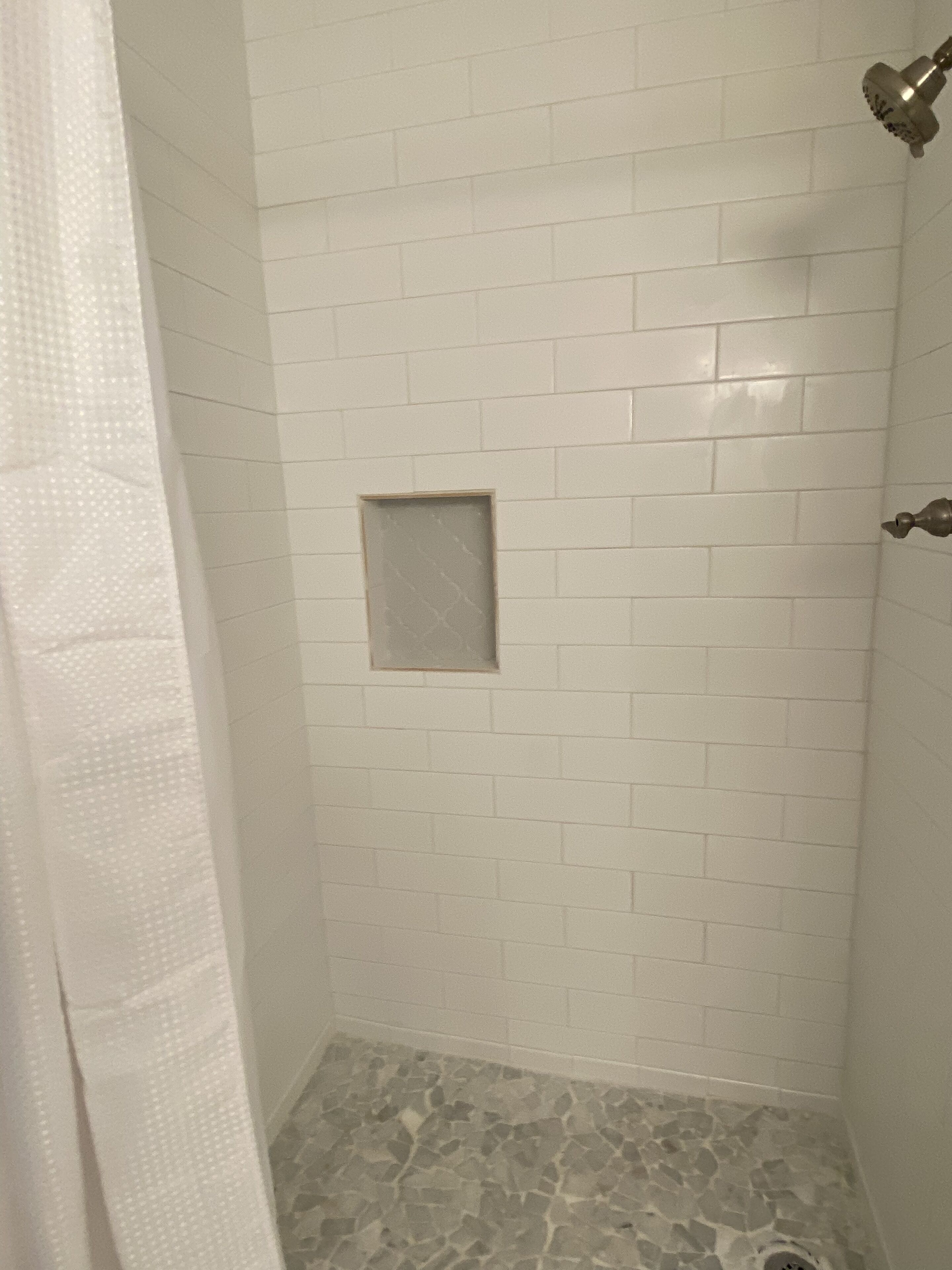 Ducha con paredes de azulejos blancos y suelo de piedra.