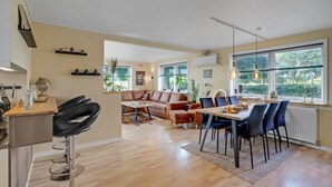 Amplia sala de estar con mesa de comedor, sillas, sofá y zona de cocina con taburete de bar.