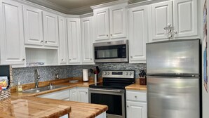 A modern kitchen with white cabinets, stainless steel appliances, and a wooden countertop. - Shore Beats Work condo @ Caribbean Dunes across from Crystal Beach - Snowbirds ❤️ (Destin)