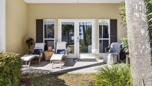 A covered patio with two lounge chairs, a fan, and a small table. - Shore Beats Work condo @ Caribbean Dunes across from Crystal Beach - Snowbirds ❤️ (Destin)