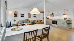 Et moderne køkken med hvide skabe, en indbygget ovn og en træbordplade. Der er et spiseområde med et hvidt bord og stole, og en lysekrone hænger over.