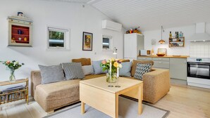 En moderne stue med sofa, sofabord og et køkkenområde med mikroovn og køleskab.